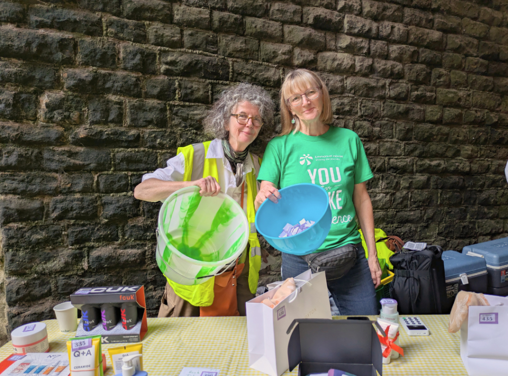 Two volunteers stood at the tombola table smiling and holding ticket buckets.