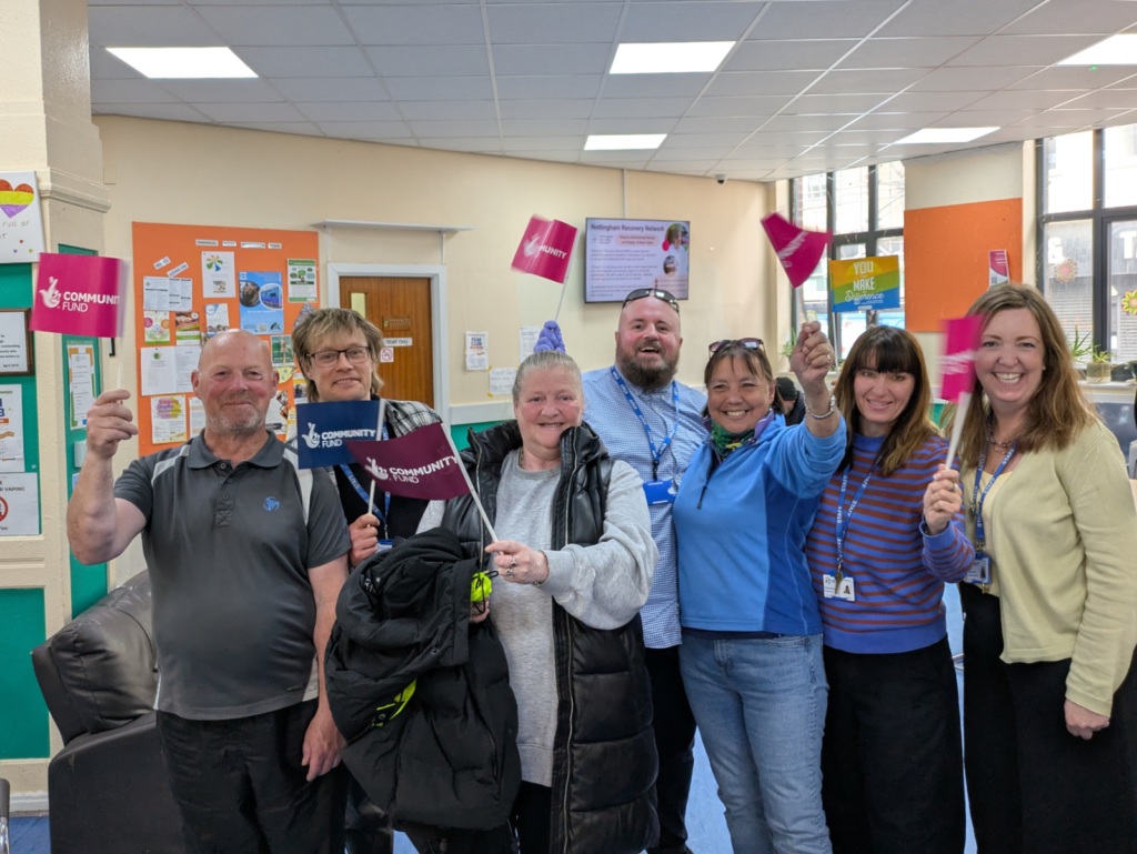 Beneficiaries and staff waving flags that say "Community Fund" with the National Lottery logo