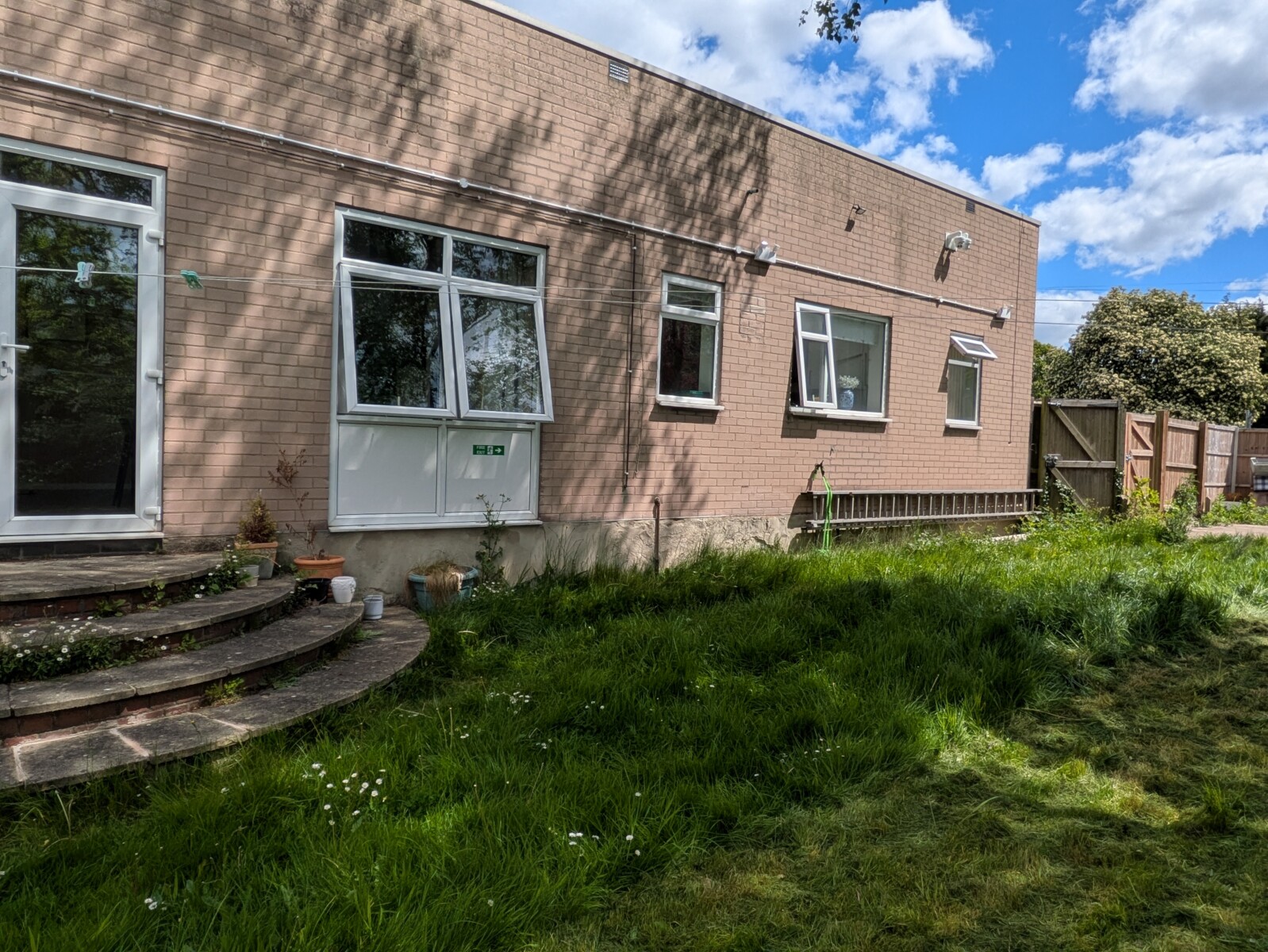 Francis House accommodation, a large one-story building, photo taken from the garden where there is a lawn of grass and daisies.